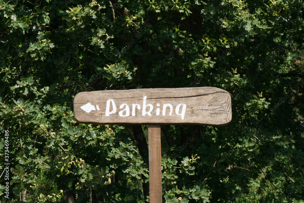 Parking wooden sign. Tourist outdoor destination arrow. Forest direction information. Summer camping in green park. Park your car over there signpost with white paint on brown desk.