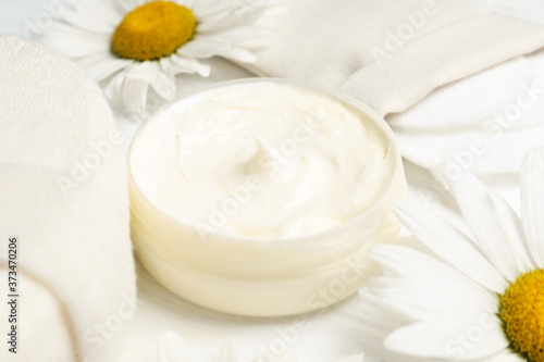 Composition with chamomile flowers and cosmetic product on white wooden table, closeup