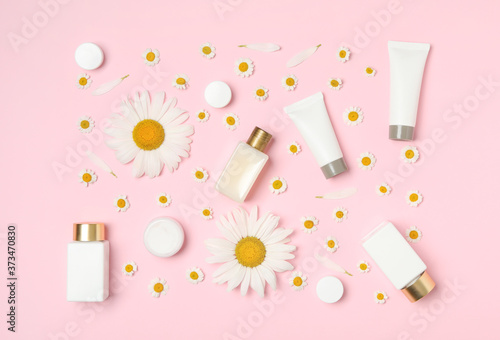 Flat lay composition with chamomiles and cosmetic products on pink background