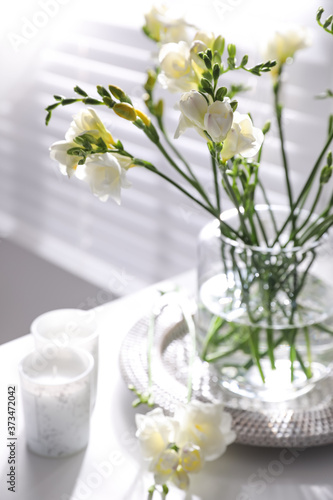 Beautiful spring freesia flowers and candles on table in room