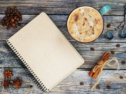 Blank craft sketchbook with cup of coffee, spoon and anise, cinnamon, beabs of coffe on vintage wooden table. Flat lay, copy space. Drawing, natural coffee substitute. Fall mockup photo