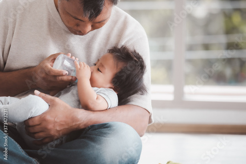 Asian father holding and feeding her baby boy with milk from baby bottle.