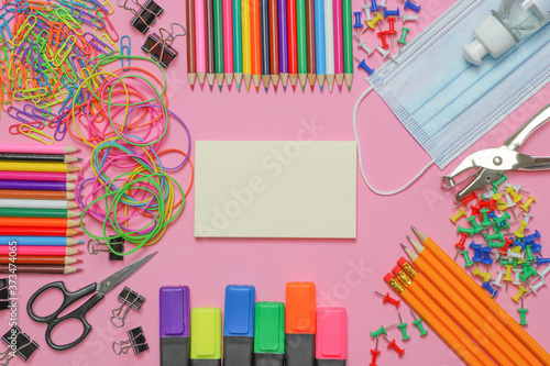 School stationery supplies with medical mask and hand sanitizer on pink background. Back to school and new normal concept. COVID-19 prevention.  Top view with copy space