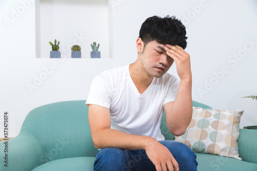 Unpleasant pain. Sad unhappy handsome man sitting on the sofa and holding his forehead while having headache