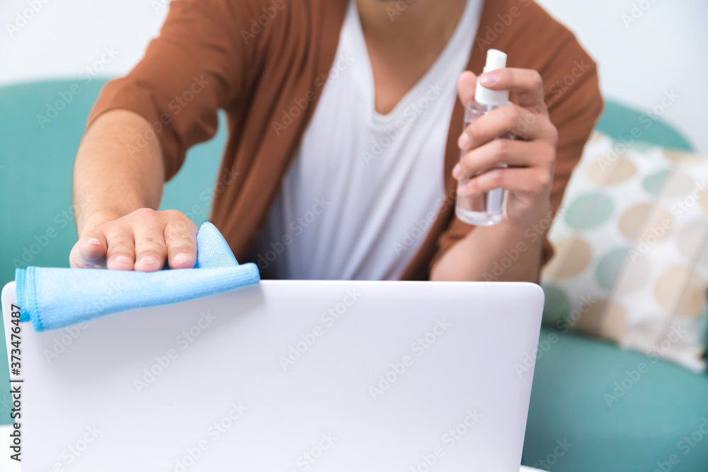 Remote job and disinfection concept. Man spraying antiseptic, cleaning laptop computer at home.