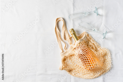 Picnic and outing concept with net or mesh bag and rose champagne on white textile background