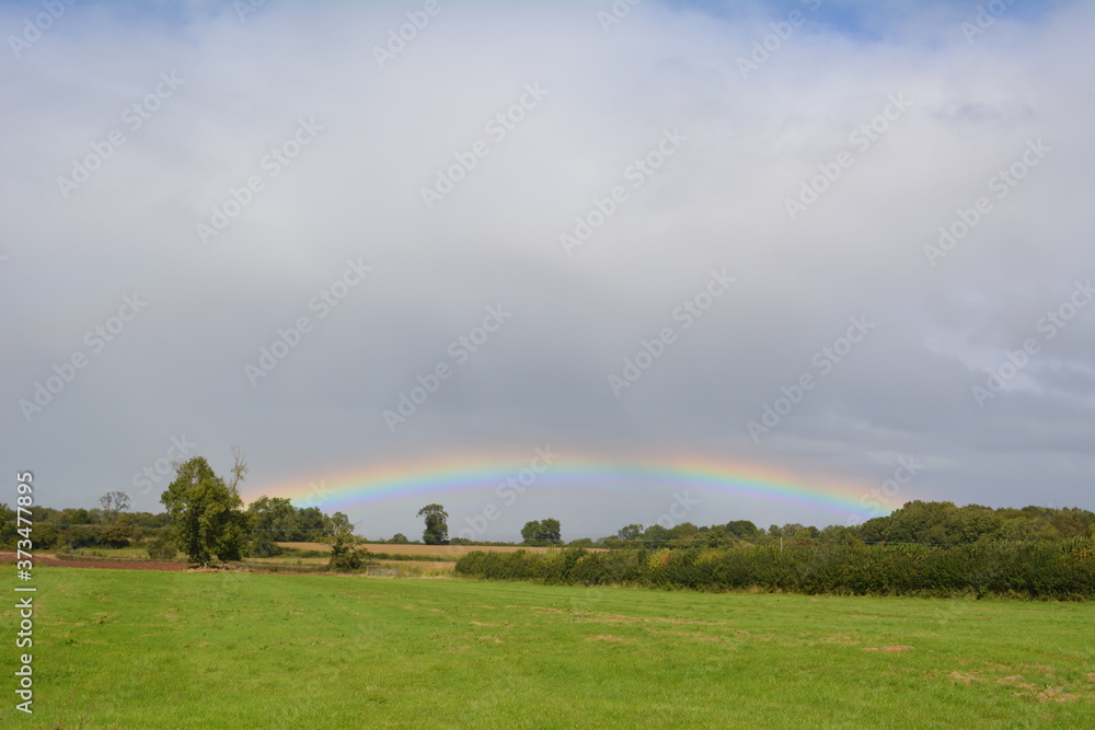 A rainbow over green fields with blue sky and clouds A rainbow over green fields with blue sky and clouds
