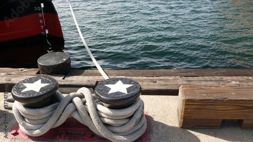 Tied rope knot on metallic bollard with stars, seafaring port of San Diego, California. Nautical ship moored in dock. Cable tie fixed on wharf. Symbol of navy marine sailing and naval fleet, USA flag © Dogora Sun