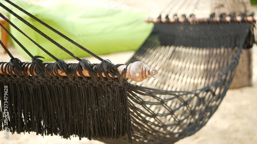 Black hammock stretching between coconut palms. Mesh vintage hipster hammock with fringe on edges stretched on sandy paradise beach of tropical island. Relax, travel vacation holiday resort concept.