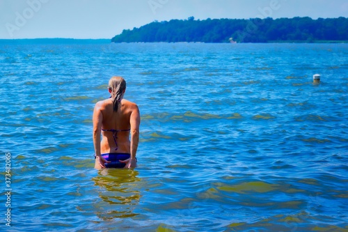 back view of blonde woman walking into the water at the beach