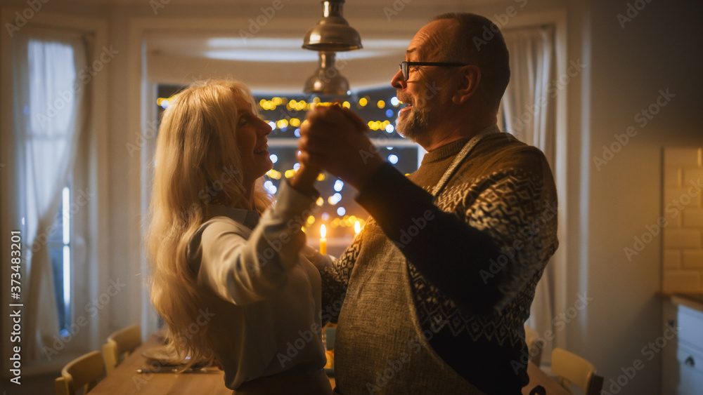 Senior Couple in Love Have Romantic Evening, Dancing in the Kitchen, Celebrating Anniversary. Portrait of a Happy Elderly Husband and Wife Have Lovely Evening with Festive Table in Cozy Kitchen