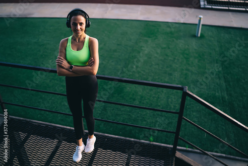 Cheerful sportswoman resting on stairs and listening to music
