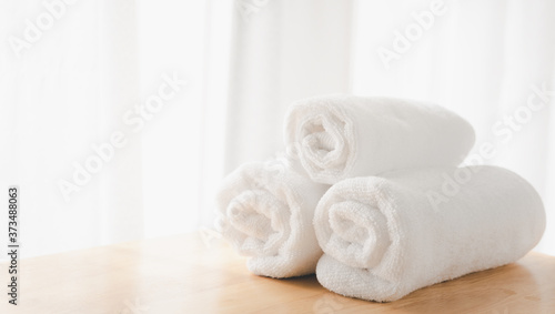 Clean white towels fold on wood table with blurred white bathroom background