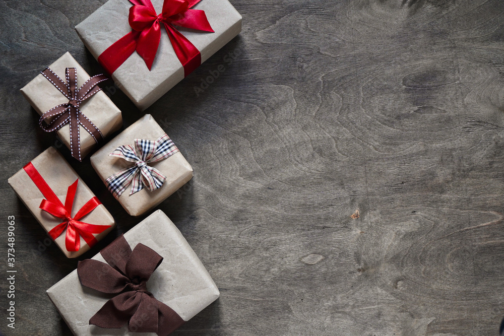 Many gift boxes wrapped in brown paper and tied with different ribbons on a wooden background, top view, copy space.Christmas and New Year concept. - obrazy, fototapety, plakaty 