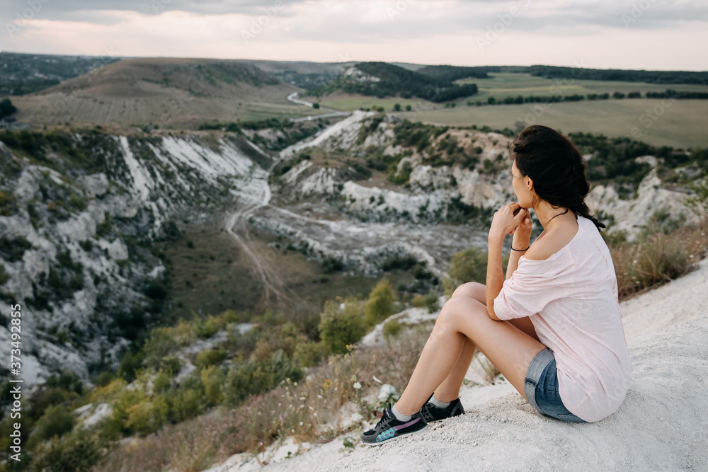 Young woman sitting on a top of a mountain, looking to a white stone canyon.