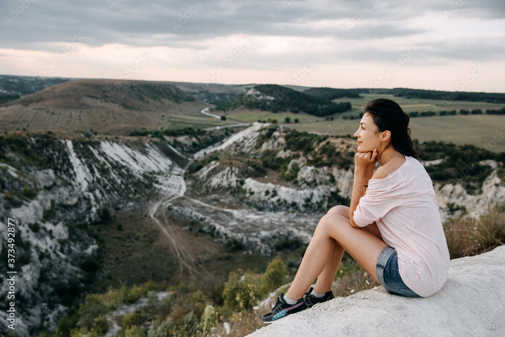 Young woman sitting on a top of a mountain enjoying landscapes.