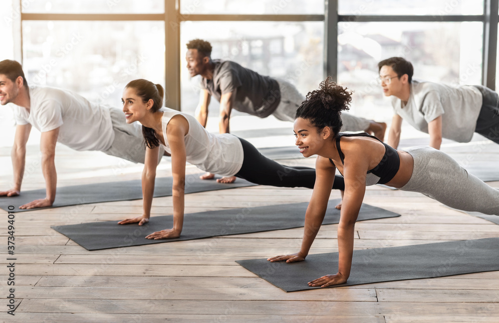 Group of sporty people practicing yoga together, standing in plank phalankasana pose Group of sporty people practicing yoga together, standing in plank phalankasana pose