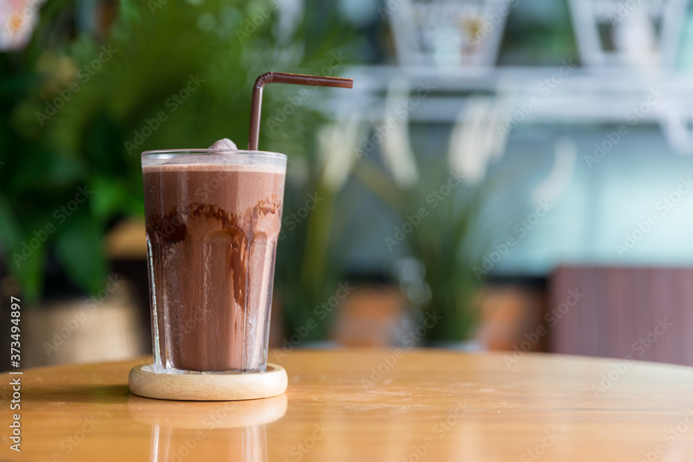A glass of iced chocolate on table. A glass of Iced Cocoa cool drink served on table. Iced cocoa drink on a wooden table at a cafe. 
