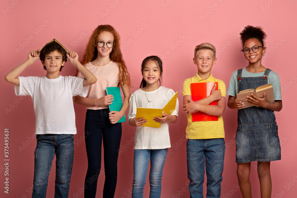 Multinational group of kids with books and notebooks ready for school on pink studio background Multinational group of kids with books and notebooks ready for school on pink studio background