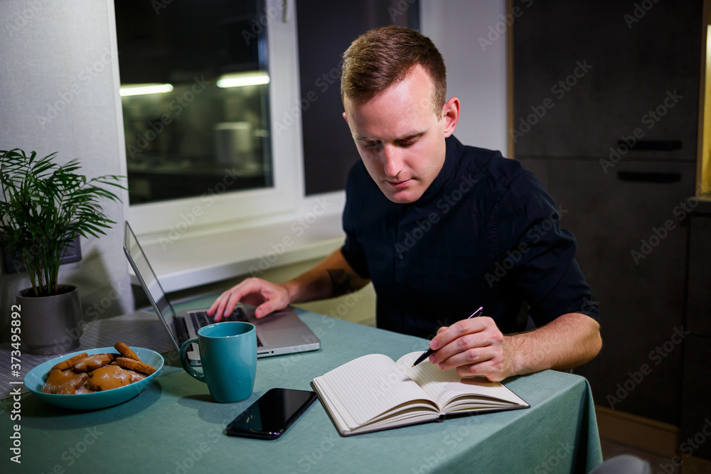 A freelancer works from home in the kitchen and using a laptop. Successful man working with a laptop and reading good news. Handsome successful entrepreneur sits and works in his modern home. A freelancer works from home in the kitchen and using a laptop. Successful man working with a laptop and reading good news. Handsome successful entrepreneur sits and works in his modern home.