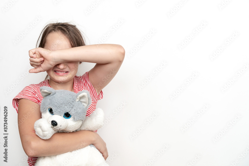 A little girl with a toy in her hands covers her face with her hands and cries on a white background. International day of non violence. A little girl with a toy in her hands covers her face with her hands and cries on a white background. International day of non violence.