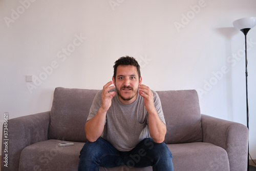 Portrait of a excited young man sitting on a sofa watching his sport team, which is about to score points. © Ladanifer
