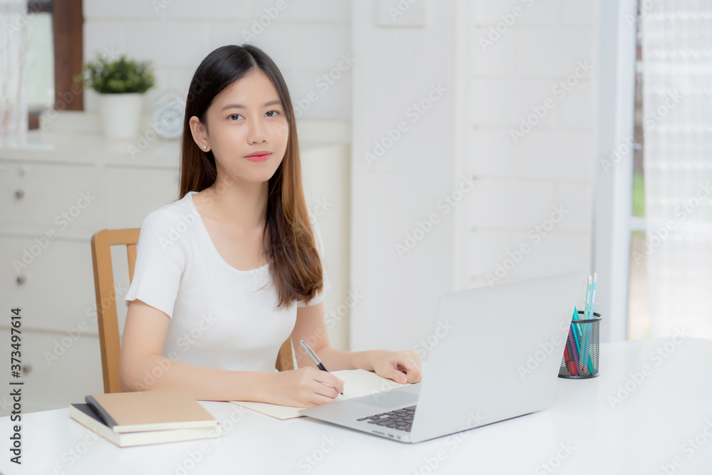 Young asian woman writing on notebook for planning working and using laptop computer on desk at home, girl notes about finance, female study and learning, business and communication concept. Young asian woman writing on notebook for planning working and using laptop computer on desk at home, girl notes about finance, female study and learning, business and communication concept.
