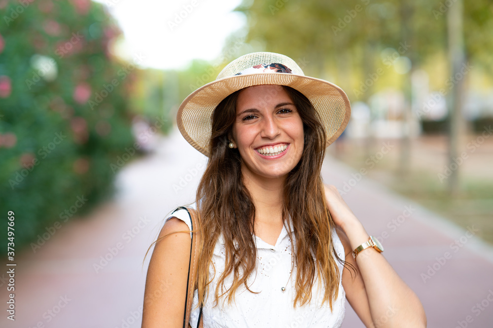 Close up portrait of an attractive young girl looking at camera smiling with a hat in the middle of the park