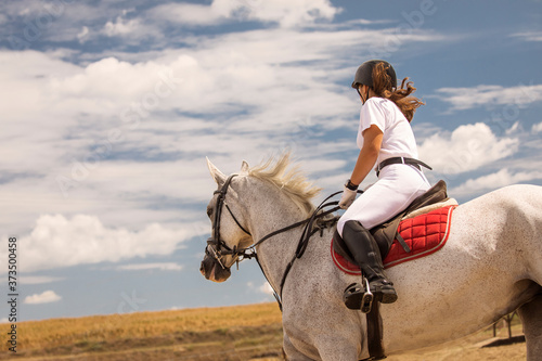 Woman enjoyng hores riding. on a white horse during a beautiful day with white clouds annd blue sky in background, full of joy photo