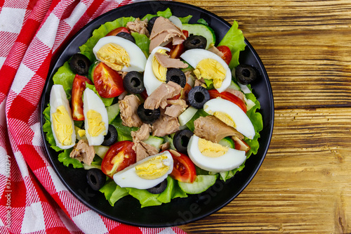 Tasty tuna salad with lettuce, black olives, eggs and fresh vegetables on wooden table. Top view