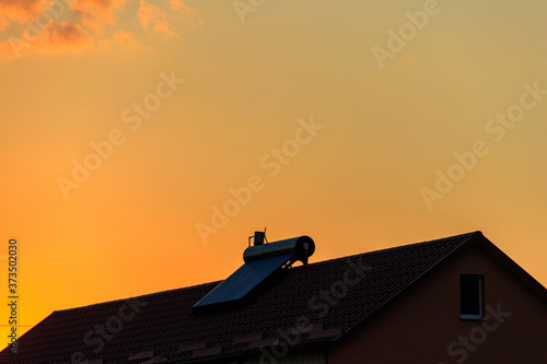 Solar water heater on a residential house rooftop at sunset. Renewable energy for house © olyasolodenko