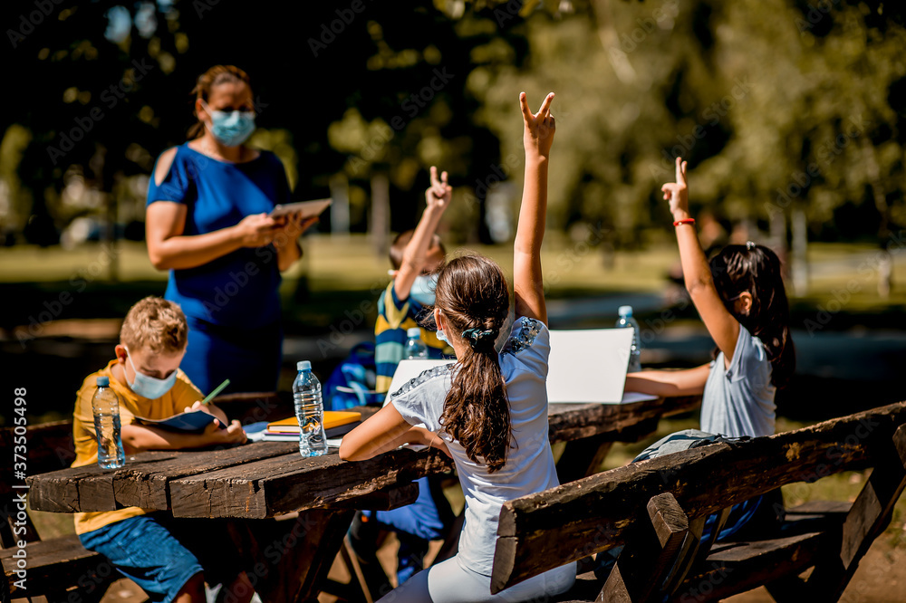 Group of school children enjoying a class with their teacher outdoors. They are wearing a protective face mask.