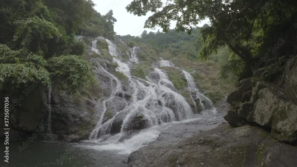 This is a close up handheld shot of a multi-tiered falls in Philippines. Surrounded by a dense forest, water sliding down cascading rocks to a dark basin on the left. This is a close up handheld shot of a multi-tiered falls in Philippines. Surrounded by a dense forest, water sliding down cascading rocks to a dark basin on the left.