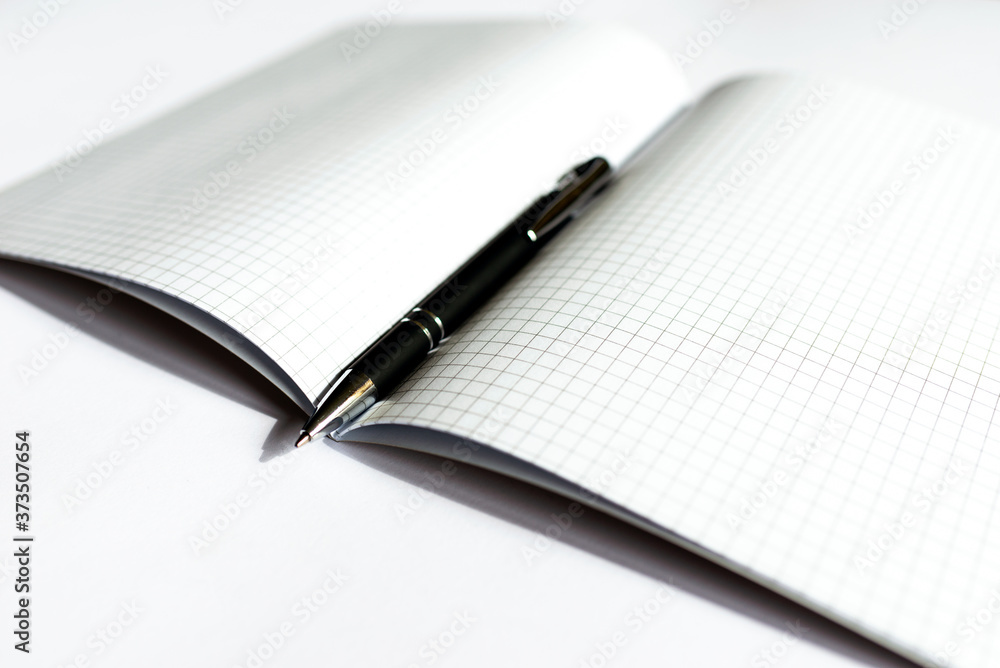 Top view Checkered notebook with a black pen on a white background. Place for text.Copy space. Top view Checkered notebook with a black pen on a white background. Place for text.Copy space.