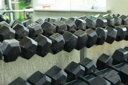 A dumbbell rack in the fitness room near a large mirror. Dumbbells on a rack. Black dumbbells for strengthening and building muscle mass.