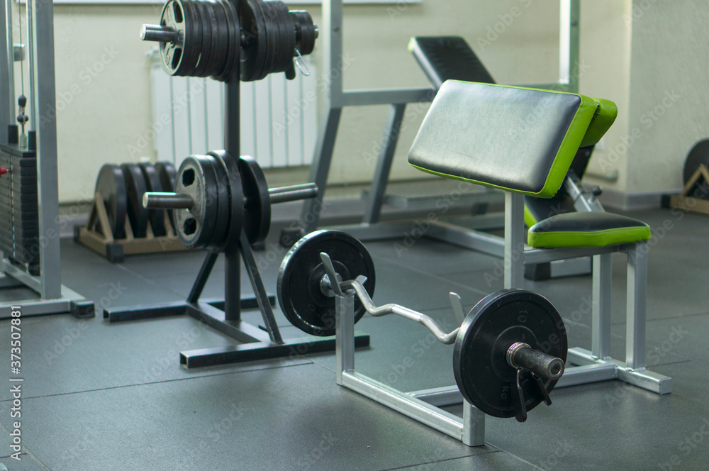 A barbell with discs and clips on a rack for training arm muscles in the fitness room. Development of the muscles of the biceps. A barbell with discs and clips on a rack for training arm muscles in the fitness room. Development of the muscles of the biceps.