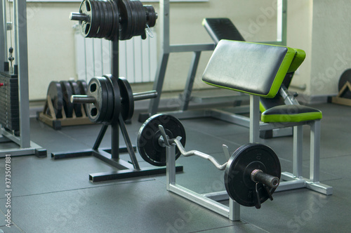 A barbell with discs and clips on a rack for training arm muscles in the fitness room. Development of the muscles of the biceps.