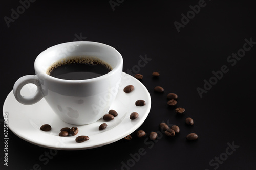 Black hot coffee in white coffee cup and saucer with beans coffee on black background.front view.