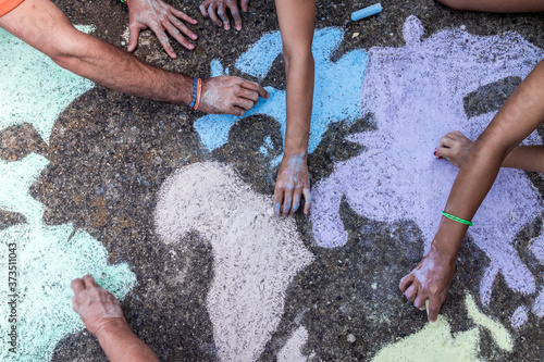 A group of people drawing with colored chalks on the floor with his hands in the street a map of the world