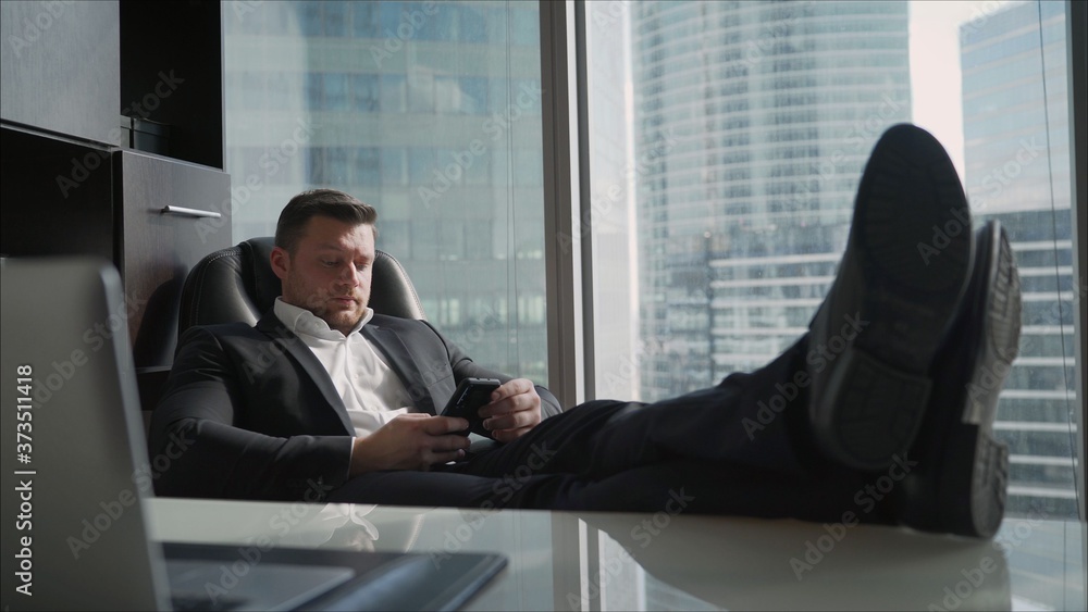 Surfing web at home. Handsome young man working on laptop and smiling while sitting in big comfortable chair at home. Successful businessman is resting while sitting in a chair behind a laptop Surfing web at home. Handsome young man working on laptop and smiling while sitting in big comfortable chair at home. Successful businessman is resting while sitting in a chair behind a laptop