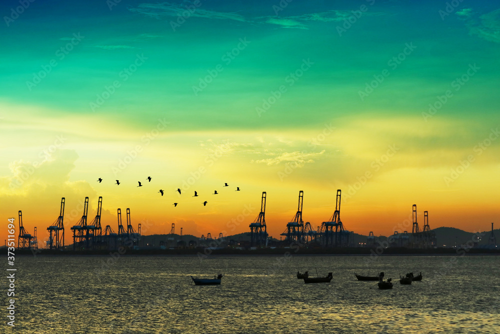 birds flying over cranes on seaport and sunset colorful sky and many fishing boats on sea