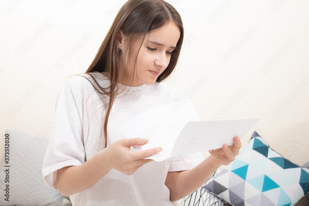 Account, notice. A girl reads a receipt of payment, a letter at home, carefully looks at the text Account, notice. A girl reads a receipt of payment, a letter at home, carefully looks at the text