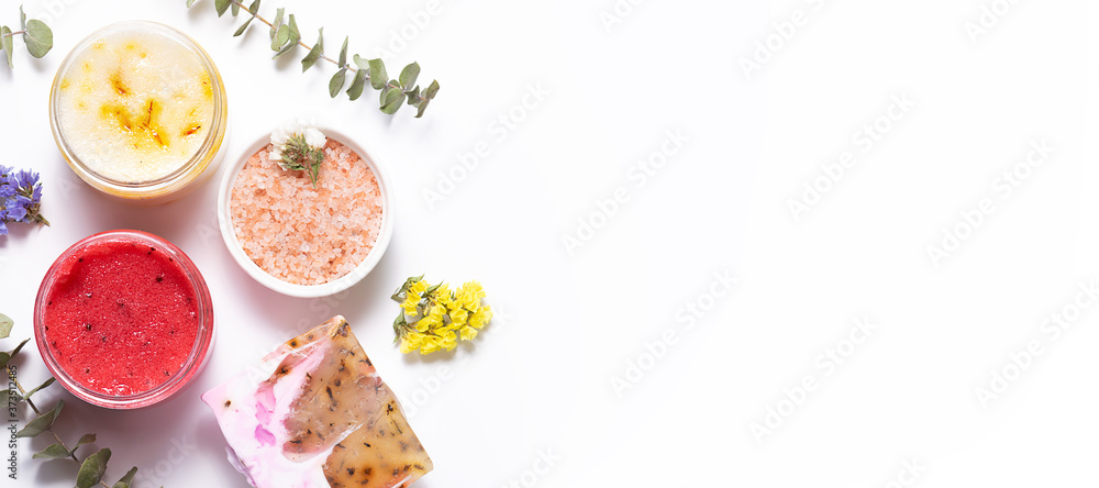 Long wide banner with natural cosmetic scrubs. handmade soap different flowers and herbs on white background. Home spa and natural cosmetic concept.