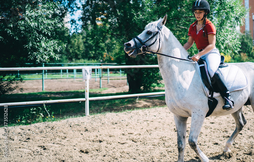 Horseback riding in saddle concept, Caucasian professional female jockey dressed in active wear and black helmet enjoying outside dressage during summer courses with beautiful mare in bridle