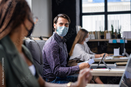 Portrait of young businesspeople with face masks working indoors in office.