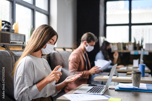 Portrait of young businesspeople with face masks working indoors in office, disinfecting hands. photo