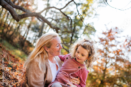 Small girl with grandmother on a walk in autumn forest, having fun.