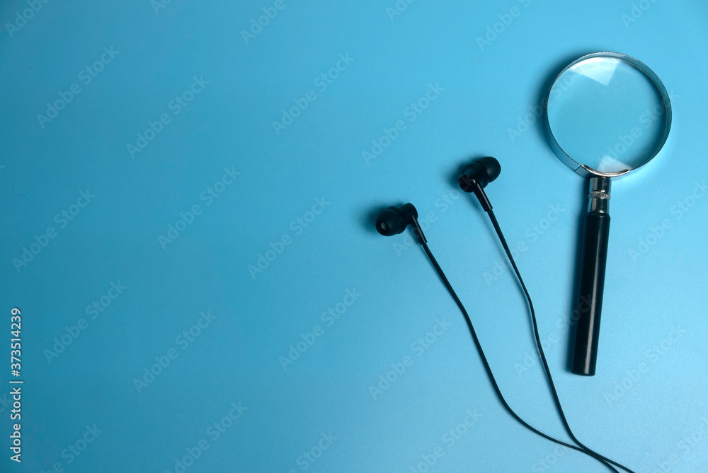 Top view of magnifying glass and earphone with copy space on a blue background. Top view of magnifying glass and earphone with copy space on a blue background.