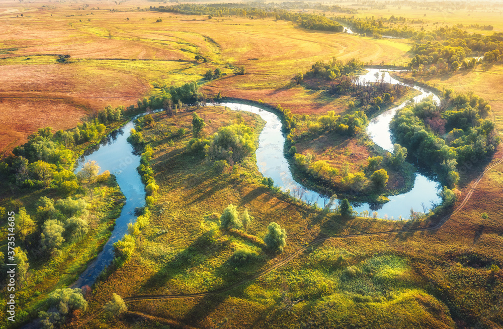 Aerial view of beautiful curving river at sunrise in summer. View from air. Turns of river, green meadows with grass and trees at dawn. Colorful aerial landscape of river coast at sunset. Top view