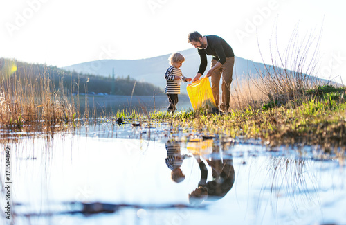 Father with small son collecting rubbish outdoors in nature, plogging concept.